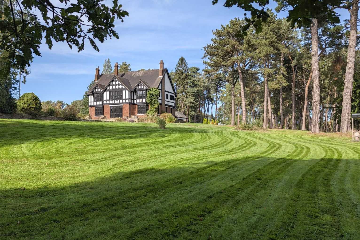 A very large striped lawn framed by trees, with a house in the distance.